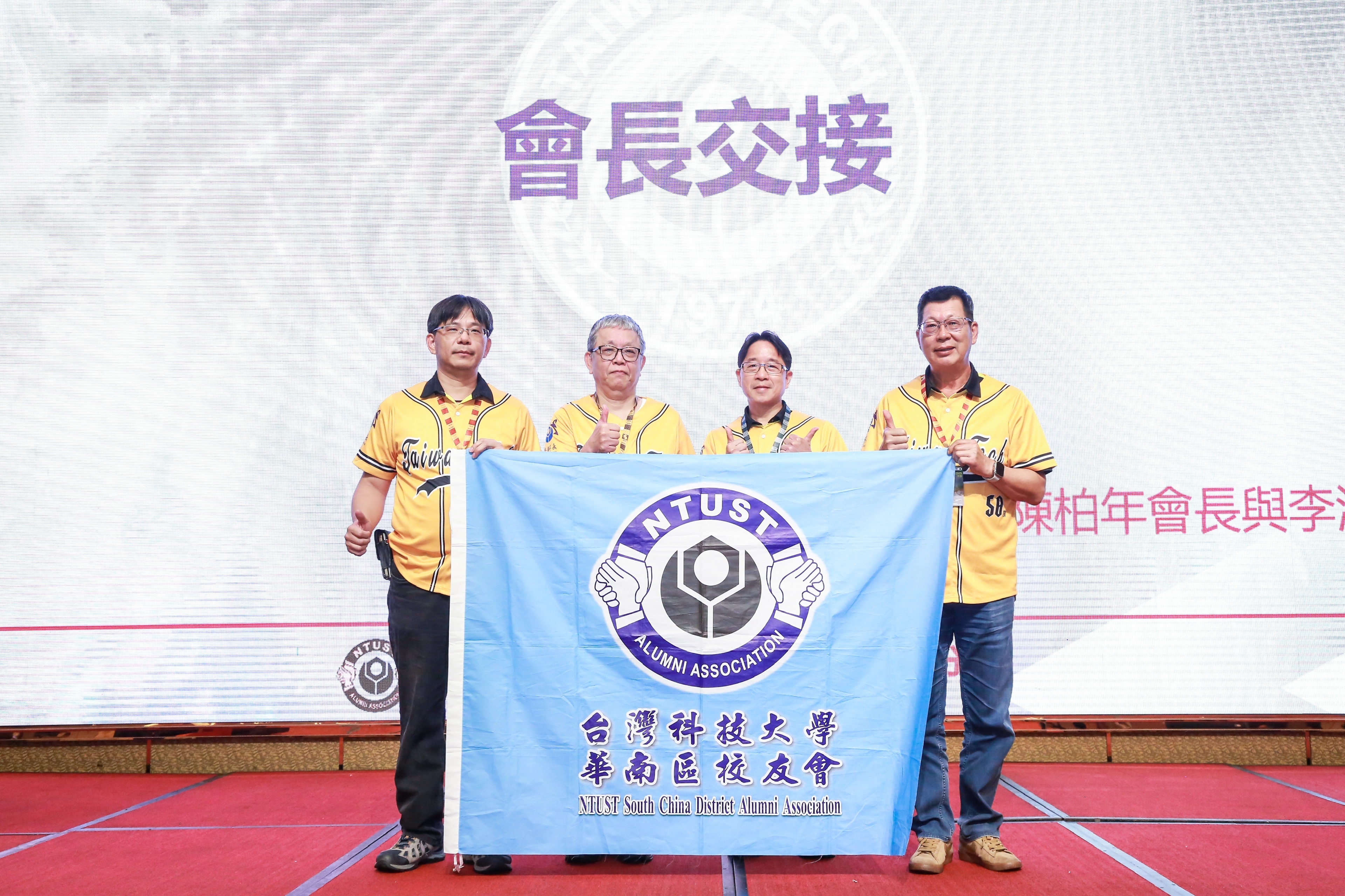 華南校友會第四屆陳柏年會長(左一)將會旗交接給第五屆李清鋒會長(右一),由臺科大周子銓副校長(右二)及蘇順豐副校長(左二)監交。